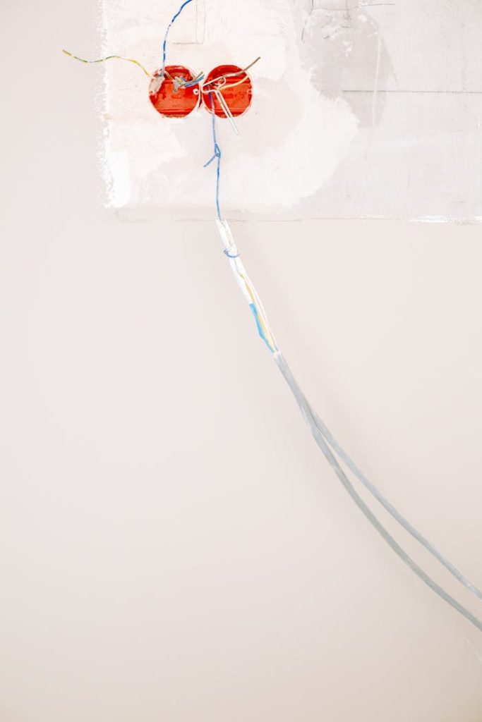 Close-up of electrical wiring installation with exposed wires against a white wall.